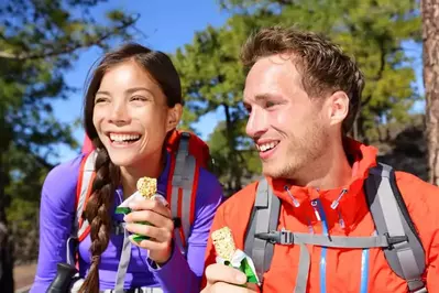 Happy couple eating granola bars on a hike.