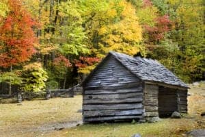 An historic cabin in Cades Cove with fall foliage in the background.
